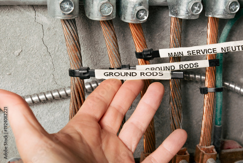 Electrical grounding and bonding busbar system. Electrician inspecting labeled grounding rods in electrical room. Copper conductors, clamps, and grounding electrodes mounted on wall. Selective focus.