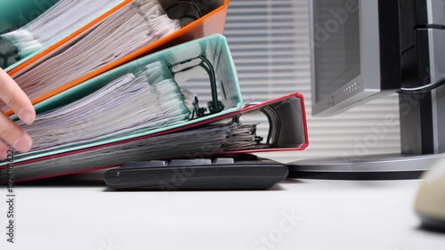 Stacked office binders overflowing with paperwork creating a feeling of being overwhelmed and signifying a heavy workload on an office desk next to a computer monitor