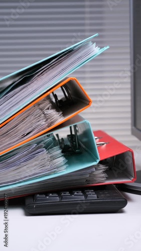 Vertical video stacked office binders overflowing with documents on a crowded desk, symbolizing bureaucratic overload and data chaos