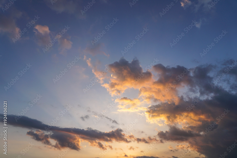 Obraz premium Stunning sunset. Dark clouds blend with bright orange and gold hues against a blue sky.