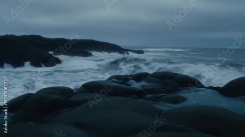 Ocean Waves Crash Against Rocky Shoreline Under Gloomy Sky