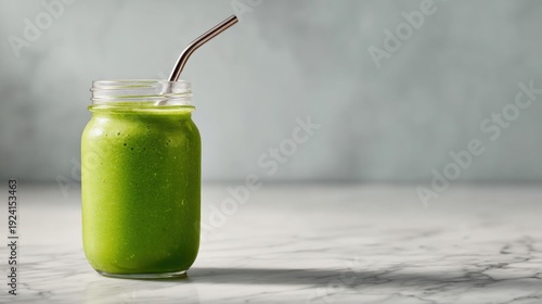 Glass jar filled with a green smoothie. the jar is made of glass and has a metal straw sticking out of the top. the smoothie appears to be a vibrant green color and is smooth and creamy.