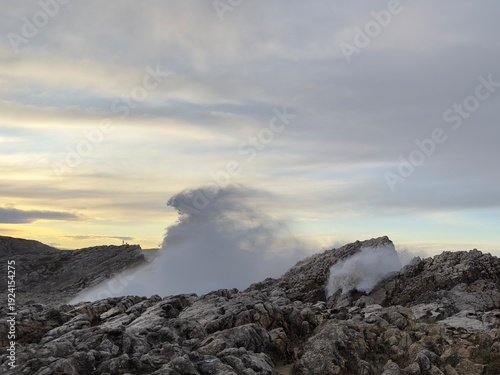 Atlantic storm wave behind rocky cliffs at Virgen del Mar with falling sea spray sliding across the rocks under layered grey sky, forming an otherworldly landscape