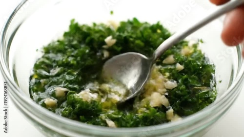 Olive oil, minced garlic, and chopped parsley mixed in glass bowl. Food preparation process in kitchen. Making a sauce or dressing ingredient.