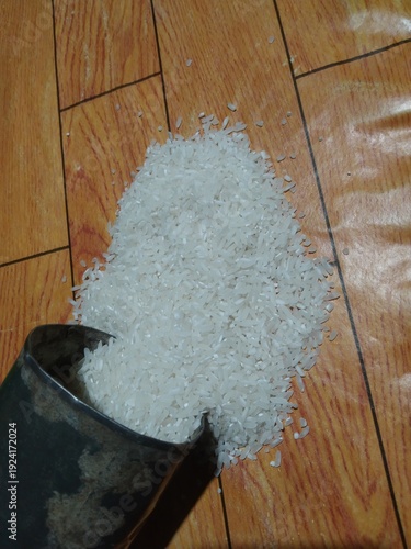 Pile of uncooked white rice spilling from a metal scoop onto a wooden surface