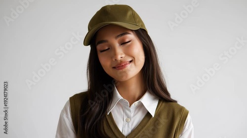 Young woman wearing a green cap and vest smiling at the camera on a plain background