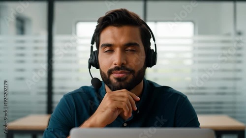 Smiling man wearing a headset sitting at a desk in an office environment with a laptop