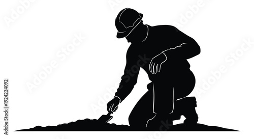 Silhouette of a construction worker kneeling and operating a tool