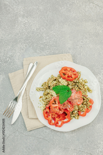 Plate of mafalda corta pasta with basil pesto, fresh tomatoes and herbs. Vegan healthy meal concept