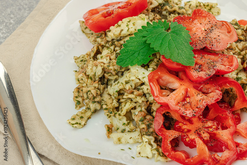 Plate of mafalda corta pasta with basil pesto, fresh tomatoes and herbs. Vegan healthy meal concept