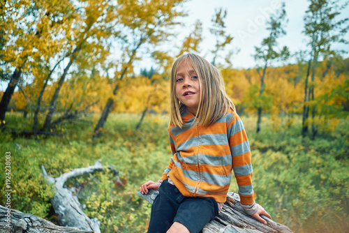 Young boy sitting on a log in the woods surrounded by fall colors