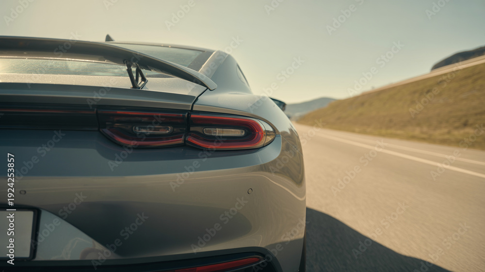Fototapeta premium Modern sleek silver sports car with aerodynamic rear spoiler driving on open highway road under bright sunlight showcasing premium automotive performance and high speed vehicle travel
