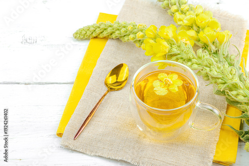 Glass cup of mullein herbal tea on natural wooden background with fresh Verbascum thapsus flowers