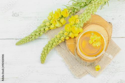 Glass cup of mullein herbal tea on natural wooden background with fresh Verbascum thapsus flowers