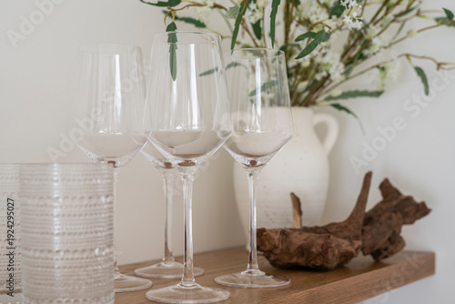 Kitchen open shelf with ceramic plates, mugs and bowls, drinking glasses and a plant. 