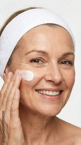 Beautiful smiling mature woman applying anti-aging facial cream on cheek, skincare for healthy skin, beauty treatments and self-care for middle-aged women.