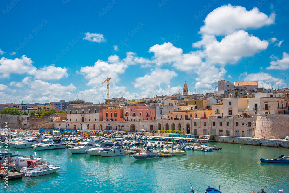 Fototapeta premium Bisceglie harbour, Puglia, southern Italy — panoramic view of the historic old town with medieval tower, fishing boats on turquoise Adriatic Sea water, and busy seafront promenade.
