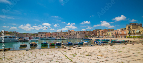 Canvastavla Bisceglie harbour, Puglia, southern Italy — panoramic view of the historic old town with medieval tower, fishing boats on turquoise Adriatic Sea water, and busy seafront promenade
