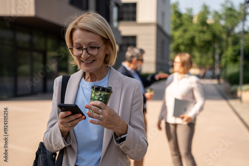Quadro su tela Portrait of happy business woman with coffee and mobile phone on her way to work on city street