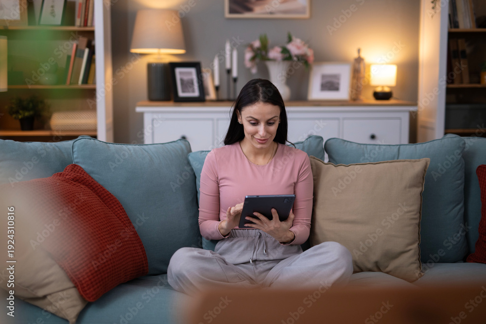 Obraz premium Woman relaxing at home using digital tablet on sofa