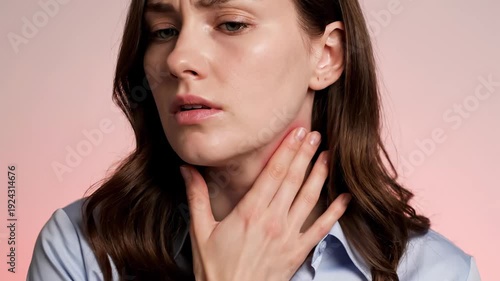 Young woman experiencing discomfort and pain, touching her red, irritated neck and throat with a concerned expression