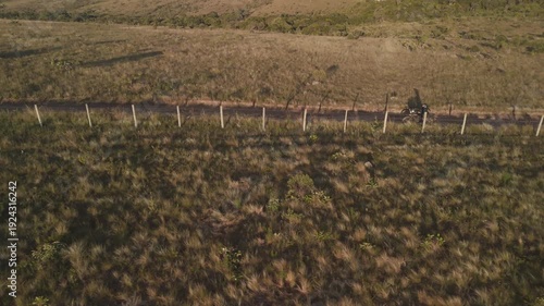 Vista aérea de uma mulher pilotando uma motocicleta em uma estrada de terra deserta no alto da montanha no nascer do sol