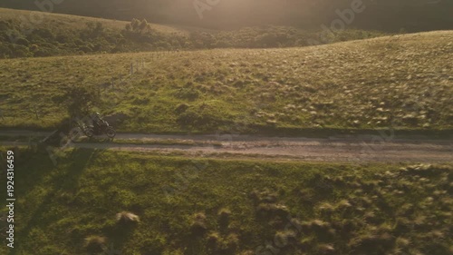 Vista aérea de uma mulher pilotando uma motocicleta em uma estrada de terra deserta no alto da montanha no nascer do sol