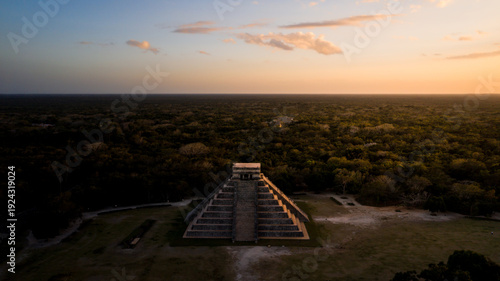 Aerial view of the ancient Mayan step pyramid El Castillo stands majestically amidst a sea of green jungle, under a warm, golden sunset sky, Chichen-Itza, Yucatan, Mexico.
