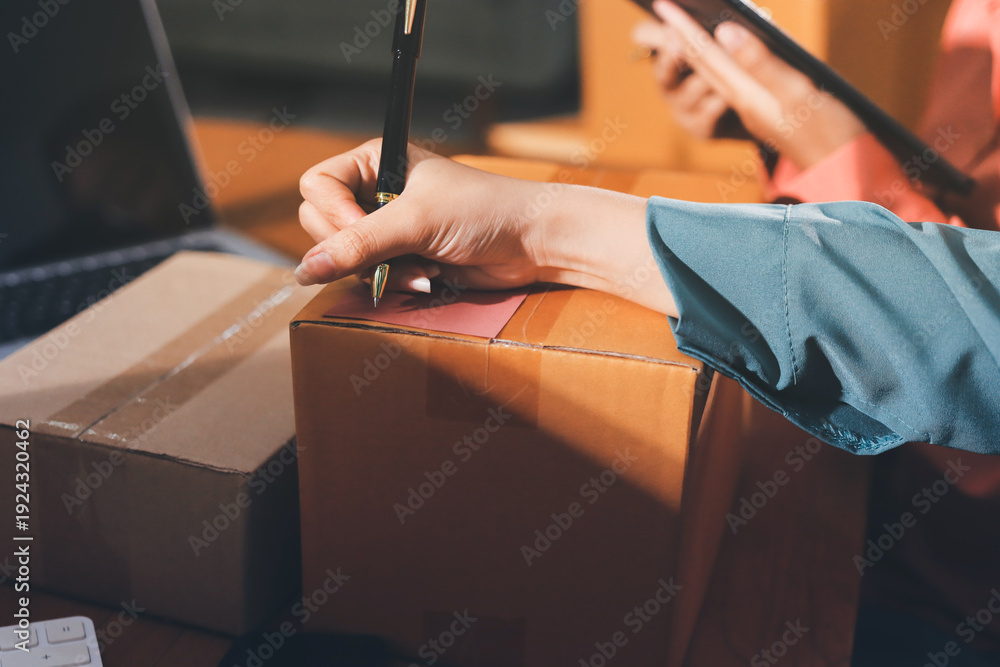 Obraz premium Startup SME small business entrepreneur of freelance Asian woman wearing apron using laptop and box to receive and review orders online to prepare to pack sell to customers, online sme business ideas.