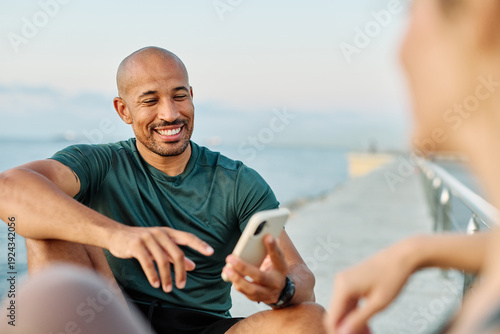 Wallpaper Mural Smiling active young couple jogging exercising and having fun and laughing together taking a breakand using a mobile phone after walking and running in the park, fitness and healhty living concept Torontodigital.ca