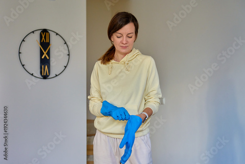 Woman standing indoors putting on blue protective gloves