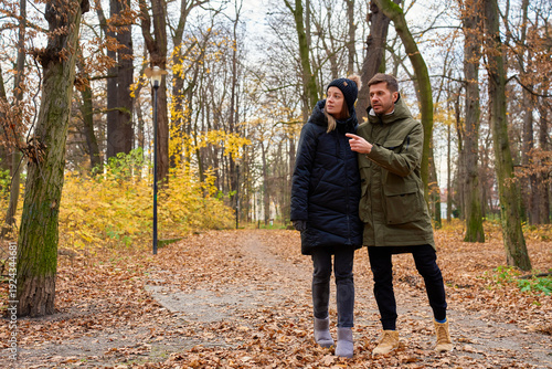 Man and woman walking together along park path covered with autumn leaves
