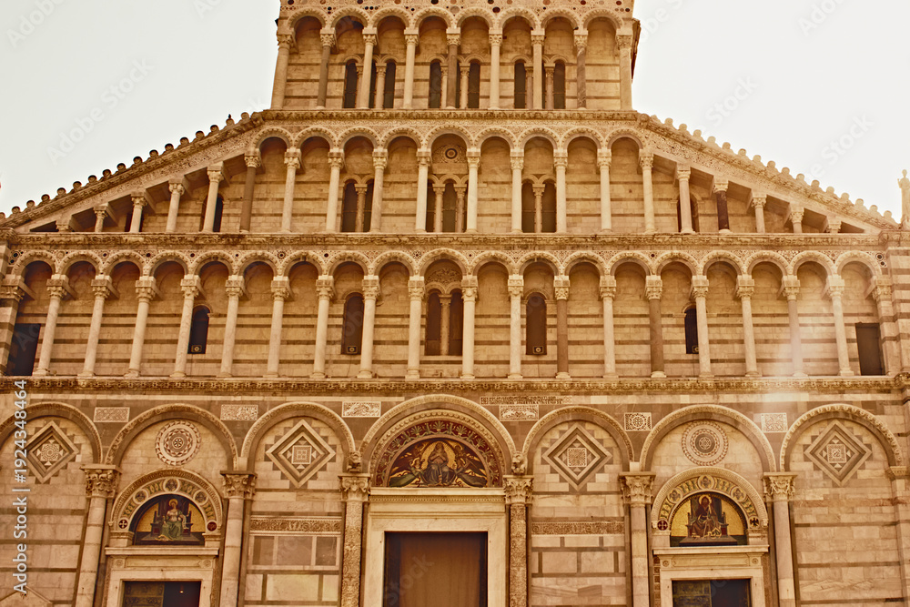 Obraz premium Historic facade of Pisa Cathedral illuminated by warm golden evening light in Pisa, Italy. Iconic European travel destination featuring Romanesque architecture, marble details and symmetrical arches. 