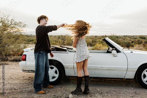 Young couple dancing in front of convertible 
