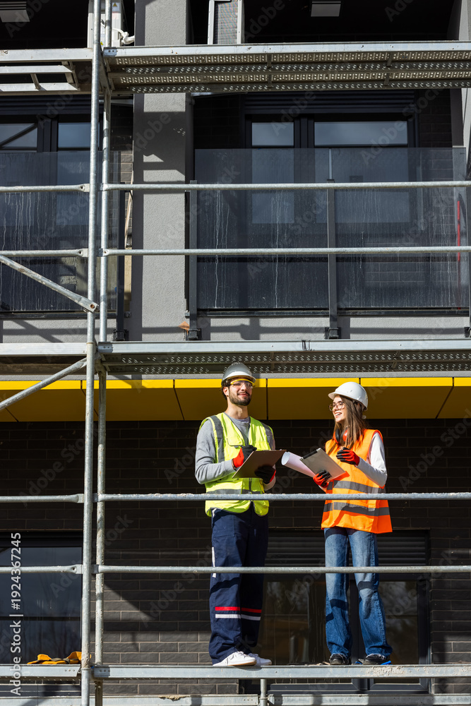 Fototapeta premium Male and female engineers reviewing project blueprints, digital tablet, and construction logbook on site.