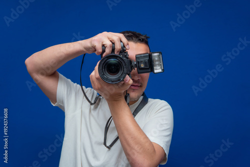 Obraz na plátně Young man holding professional digital camera with attached flash, taking a pict