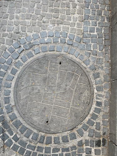 Top-down view of grey manhole cover in grey brick road showing map of 