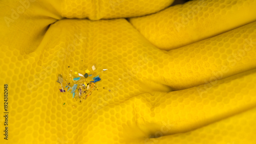 Close-up of a yellow honeycomb-textured glove holding tiny microplastic fragments and glitter, highlighting pollution and environmental contamination. Microplastic fragments on yellow protective glove