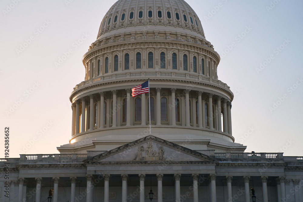 Fototapeta premium Last beams of golden sunlight on the United States Capitol Building in Washington, DC, with the American flag waving. Dramatic view