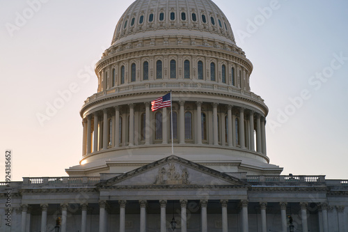 Last beams of golden sunlight on the United States Capitol Building in Washington, DC, with the American flag waving. Dramatic view