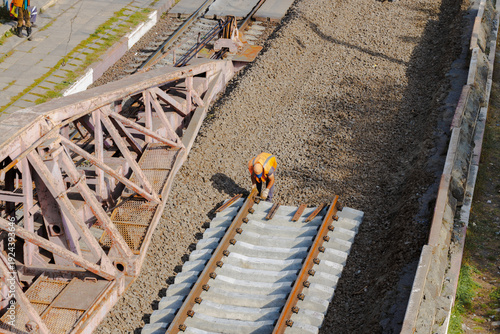Railroad worker in high-visibility vest laying new concrete railway sleepers and tracks
