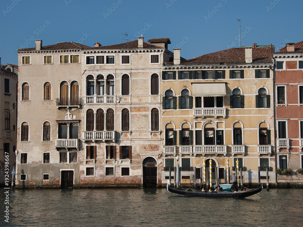 Naklejka premium Grand Canal Palaces Facades on a Clear Day - A row of historic Venetian palazzi facades along the Grand Canal with arched windows, balconies, and water access points under a clear sky.