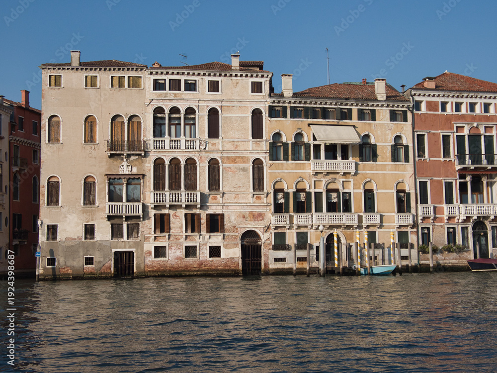 Fototapeta premium Grand Canal Palaces Facades on a Clear Day - A row of historic Venetian palazzi facades along the Grand Canal with arched windows, balconies, and water access points under a clear sky.