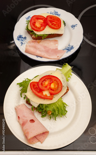 Two Open-face Sandwiches with Ham, Cheese, Tomatoes and Lettuce on Plates.