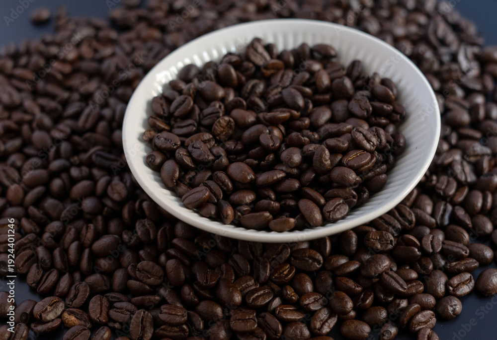 Fototapeta premium Roasted coffee beans in a white ceramic bowl on a dark background, top view.