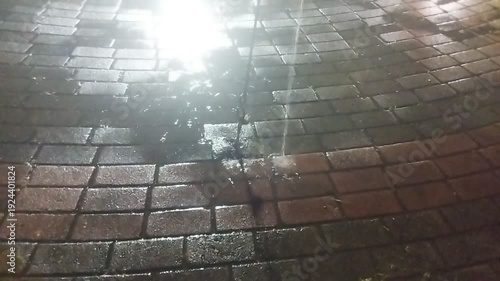 Abstract puddle with shimmering reflection on a wet city street surface during a night rain.