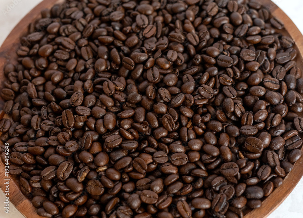 Fototapeta premium Close up of roasted coffee beans in a wooden bowl on a light surface.