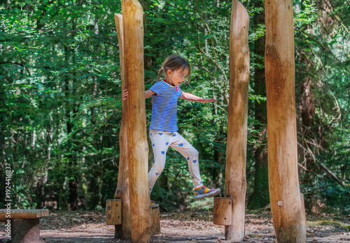 Girl balancing on wooden posts in forest playground at summer