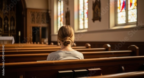 A woman sits alone in a church with stained glass windows and wooden pews.