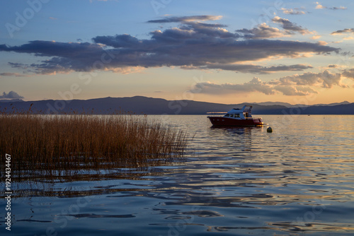 Valokuva A golden sunset casts a warm glow over Lake Ohrid, illuminating a red and white boat on the tranquil waters